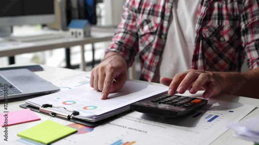 Asian male finance staff is calculating by using a calculator. Investment results to report to his boss at the meeting. On the table in the office, is the concept of calculating investment results. Asian male finance staff is calculating by using a calculator. Investment results to report to his boss at the meeting. On the table in the office, is the concept of calculating investment results.