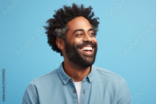 Portrait of a happy african american man laughing and looking away against blue studio background
