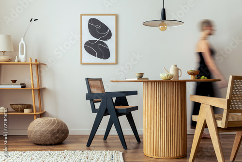 Bild auf Leinwand Warm and cozy interior of living room space with mock up poster frame, round table, rattan chairs, pedant lamp and walking young woman