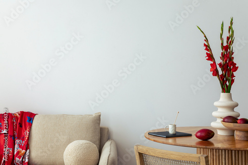Warm and cozy interior of living room space with round wooden table, beige sofa, red flowers, kimono, rattan chair, decoration. Home decor. Template. © FollowTheFlow