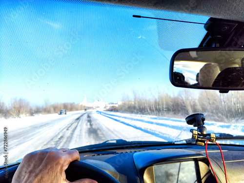 Hand of woman on the steering wheel in a car and view through the windshield of a winter road with snow-covered trees