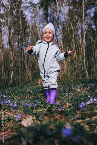 Little girl in violet boots and blue overall walking in spring blooming forest photo