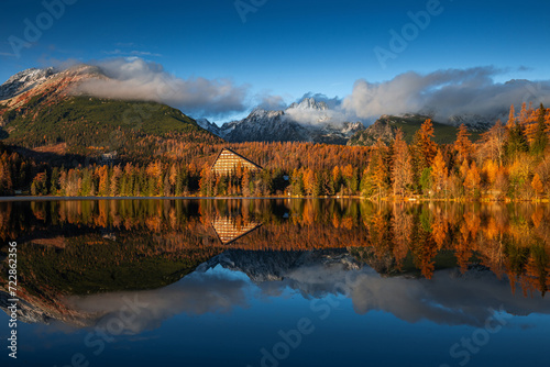 Strbske Lake, Slovakia - Panoramic view of reflecting Strbske Lake on a sunny autumn afternoon with High Tatras and Tatras Tower at background. Warm autumn colors, blue sky and blue cloudy sky