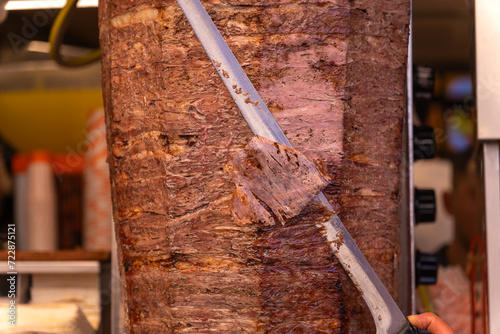 Close-up of a chef cutting meat with a doner knife for a traditional street food doner kebab or shawarma. Concept of street food