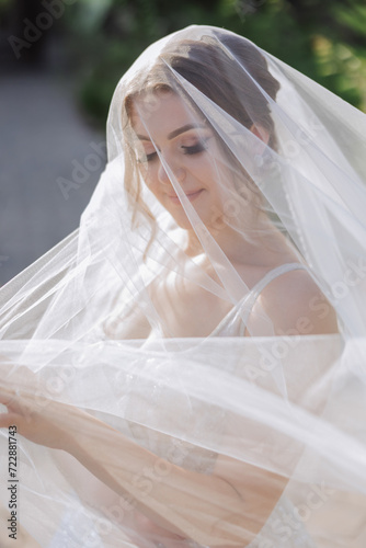 portrait of a beautiful young bride in a white dress with a long veil and a gorgeous hairstyle. Smiling bride. Wedding day. Gorgeous bride. Marriage. © Vasil