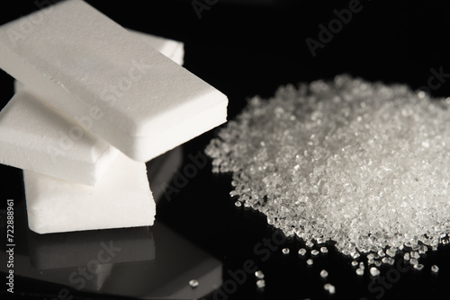 A stack of dextrose glucose tablets and a pile of white granulated sugar on black glass.