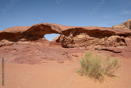 A striking rock formation natural arch stands tall amidst the vast expanse of the Wadi Rum desert in Jordan.