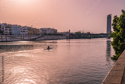 Guadalquivir river with silhouette of a canoeist, architecture of city, Isabel II bridge and Seville tower in the background at evening, SPAIN photo