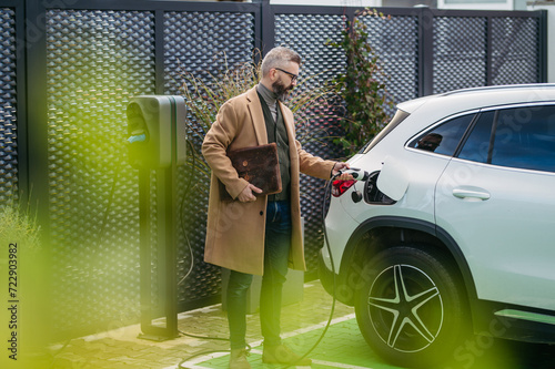 Businessman charging electric car before going to office. An electric vehicle charging station in front of office building. Charging at work, workplace. photo