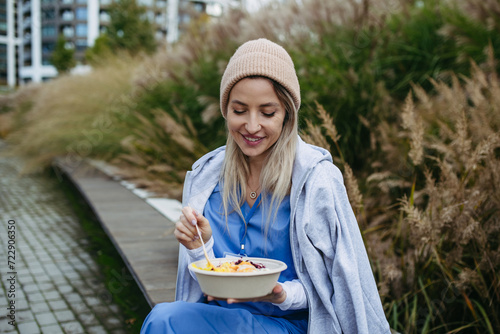 Nurse having healthy lunch, snack in front of hospital building, taking break from work. Importance of breaks in healthcare. photo