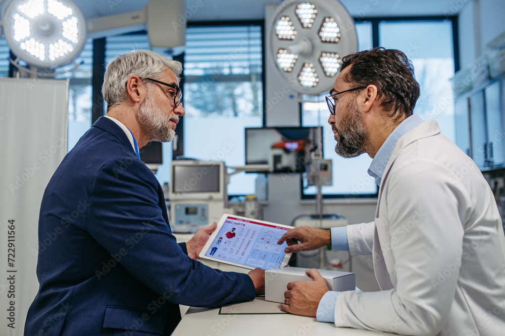 Pharmaceutical sales representative presenting new medication to doctor in medical building, holding box with medication samples. Pharmaceutical sales representative presenting new medication to doctor in medical building, holding box with medication samples.