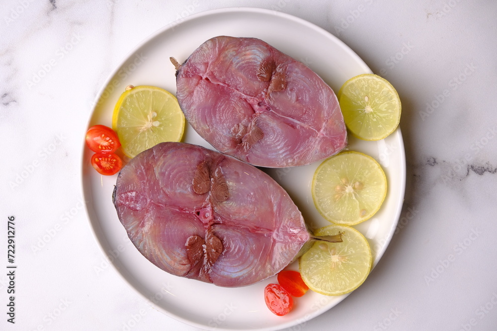 tuna cutlet steak on white ceramic plate on a white marble table. raw tuna with lemon sliced and cherry tomatoes. seafood sources of animal protein. tuna cutlet steak on white ceramic plate on a white marble table. raw tuna with lemon sliced and cherry tomatoes. seafood sources of animal protein.
