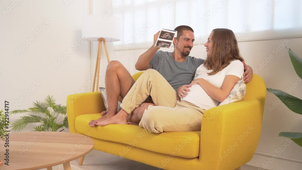 Couple expecting a baby pregnant looking at ultrasound happy relaxed on the couch at home. Couple expecting a baby pregnant looking at ultrasound happy relaxed on the couch at home.