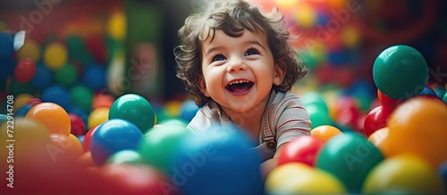 Fototapeta Happy laughing boy 1 2 years old having fun in ball pit on birthday party in kids amusement park and indoor play center in playground ball pool Activity toys for little kid. Creative Banner