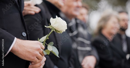 Hands, rose and a person at a funeral in a cemetery in grief while mourning loss at a memorial service. Death, flower and an adult in a suit at a graveyard in a crowd for an outdoor burial closeup photo