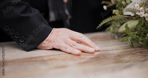 Death, funeral and hand on coffin in mourning, family at service in graveyard or church for respect. Flowers, loss and people at wood casket in cemetery with memory, grief and sadness at grave burial photo
