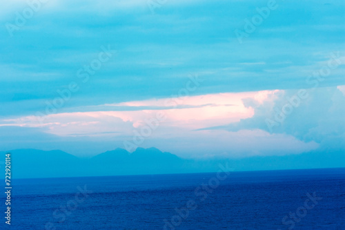 Bizarre formation of clouds in a pale blue sky over the sea.  photo