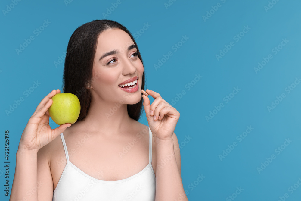 Beautiful young woman with vitamin pill and apple on light blue background. Space for text Beautiful young woman with vitamin pill and apple on light blue background. Space for text