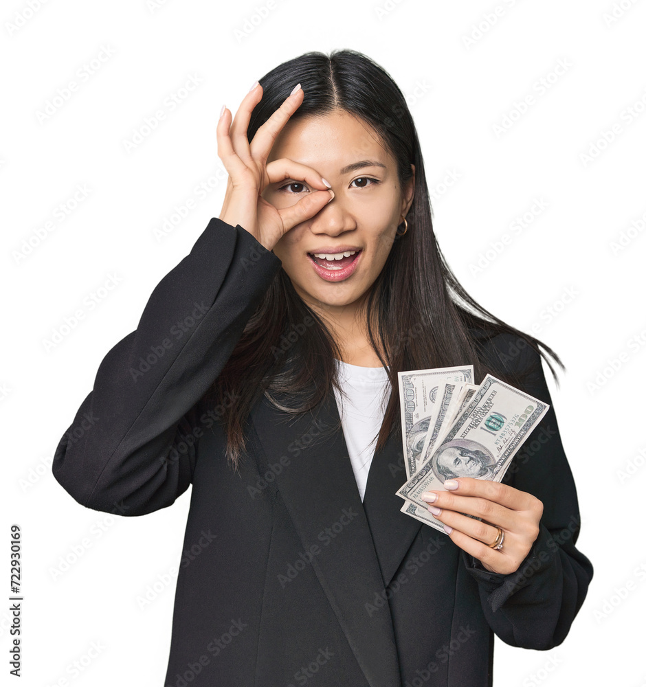 Young Chinese woman with dollars in suit excited keeping ok gesture on eye. Young Chinese woman with dollars in suit excited keeping ok gesture on eye.