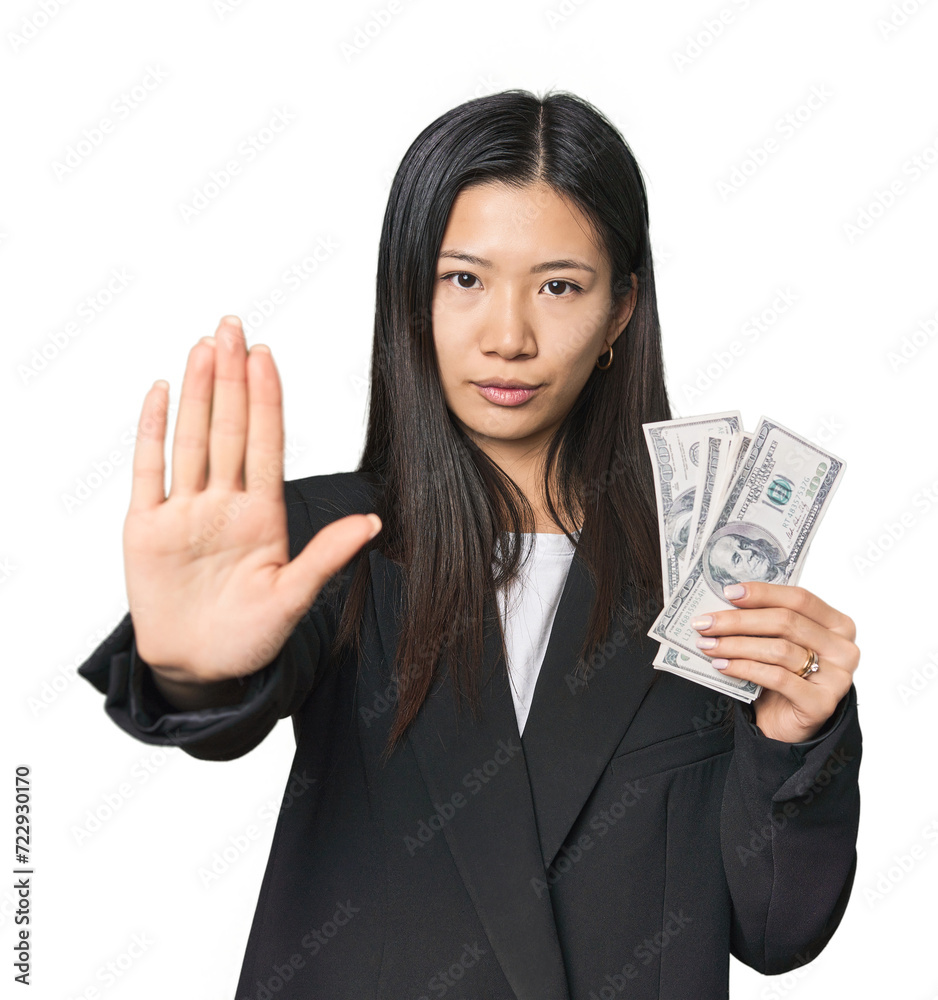Young Chinese woman with dollars in suit standing with outstretched hand showing stop sign, preventing you. Young Chinese woman with dollars in suit standing with outstretched hand showing stop sign, preventing you.