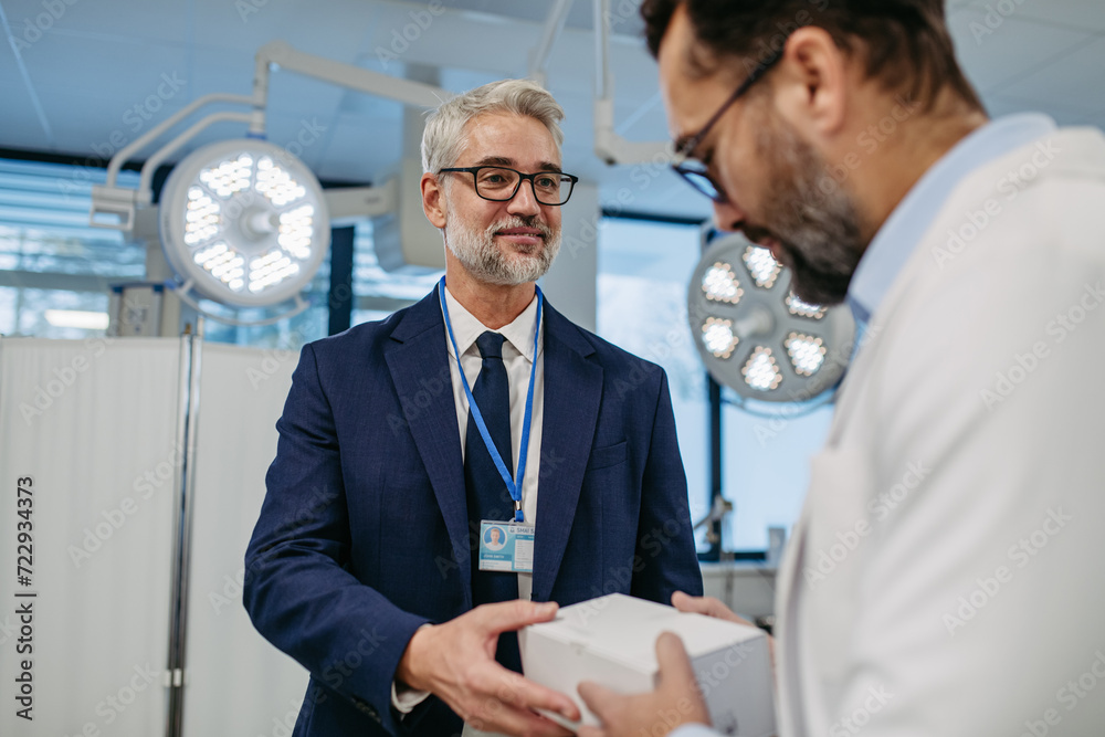 Pharmaceutical sales representative presenting new medication to doctor in medical building, holding box with medication samples. Pharmaceutical sales representative presenting new medication to doctor in medical building, holding box with medication samples.