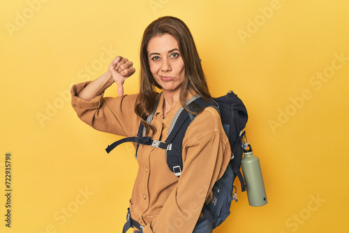 Middle aged woman prepped for hiking, yellow studio shot showing a dislike gesture, thumbs down. Disagreement concept.