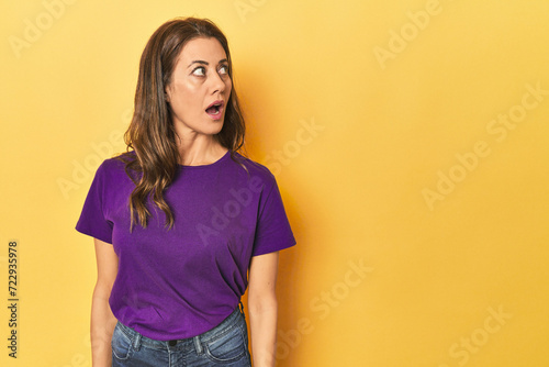 Middle-aged caucasian woman on yellow being shocked because of something she has seen.