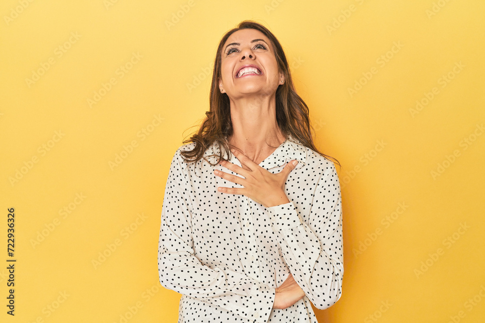 Obraz premium Middle-aged caucasian woman on yellow laughs out loudly keeping hand on chest.