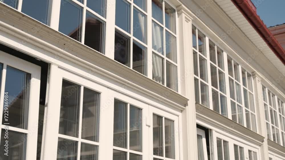 Angled view of a building facade with multiple white-framed windows, a clear sky, and architectural details, suggesting urban environment and design. Angled view of a building facade with multiple white-framed windows, a clear sky, and architectural details, suggesting urban environment and design.
