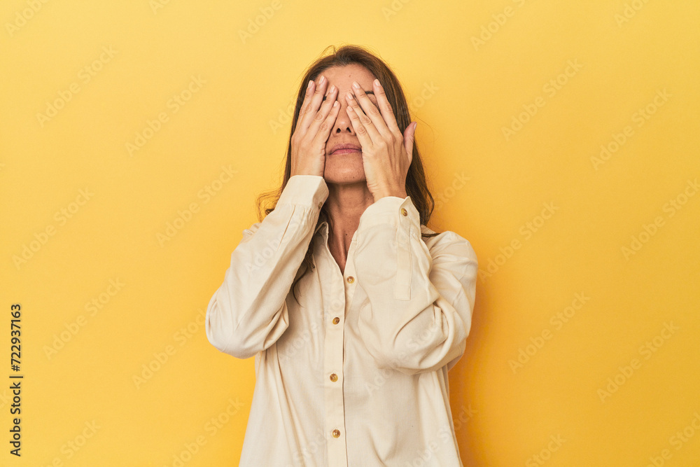 Middle-aged caucasian woman on yellow afraid covering eyes with hands. Middle-aged caucasian woman on yellow afraid covering eyes with hands.