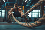 Athletic young man with battle rope doing exercise in functional training fitness gym