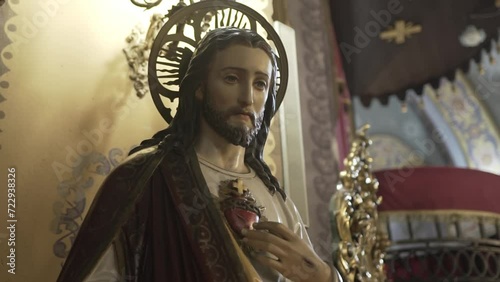 Statue of Jesus with a sacred heart, halo, and robe inside a church, with ornamental details and soft lighting enhancing its spiritual ambiance.