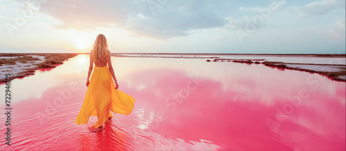 une femme blonde vue de dos marche dans des marais salants de couleur rose