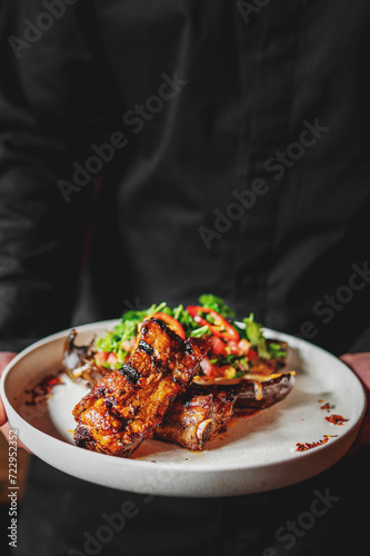 chef or waiter hold plate of grilled pork ribs with baked eggplant