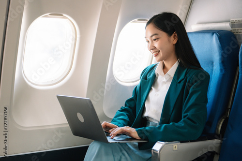 Attractive Asian female passenger of airplane sitting in comfortable seat while working laptop and tablet with mock up area using wireless connection. photo