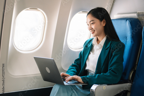 Attractive Asian female passenger of airplane sitting in comfortable seat while working laptop and tablet with mock up area using wireless connection.