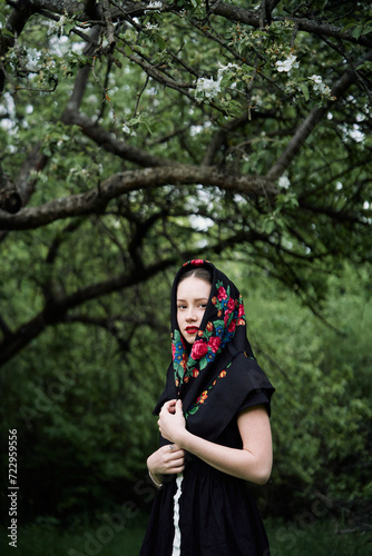 Slavic girl in a scarf near blooming apple trees