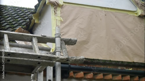 Portable scaffolding with attached ladders being moved away from a prepared work area, namely a roof dormer window, masked off with paper and tape, ready for rendering of the exposed parts. photo