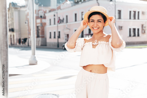 Young beautiful smiling hipster woman in trendy summer costume clothes. Carefree female posing in the street at sunny day. Positive model outdoors at sunset. Cheerful and happy in hat