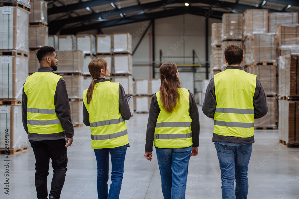 Obraz premium Rear view of warehouse workers walking in warehouse. Team of warehouse workers preparing products for shipment.