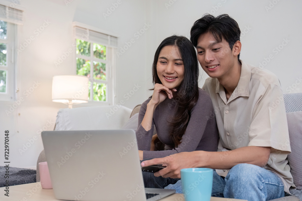 Asian couple watching movies on the internet using laptop at home Smiling Thai man and woman sitting on sofa, hugging each other, looking at computer screen. Surf the web together copy space Asian couple watching movies on the internet using laptop at home Smiling Thai man and woman sitting on sofa, hugging each other, looking at computer screen. Surf the web together copy space