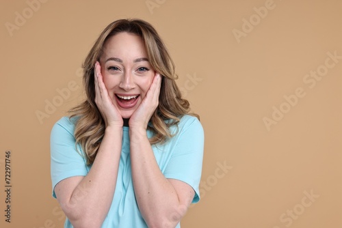Portrait of happy surprised woman on beige background. Space for text