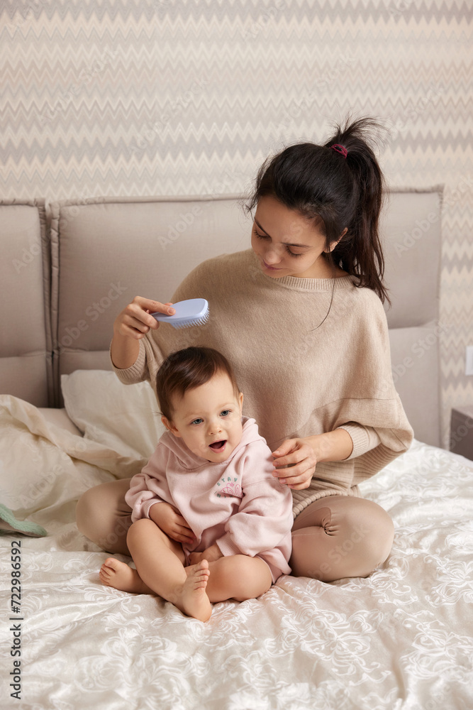 Charming mother is brushing her cute little daughter hair on bed Charming mother is brushing her cute little daughter hair on bed