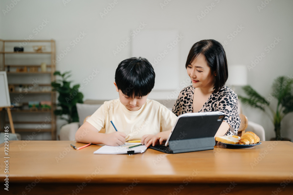 Homeschool Asian young little boy learning online and does homework by using computer and tablet with mother help, teach and encourage. son smile to study at home together with mom Homeschool Asian young little boy learning online and does homework by using computer and tablet with mother help, teach and encourage. son smile to study at home together with mom