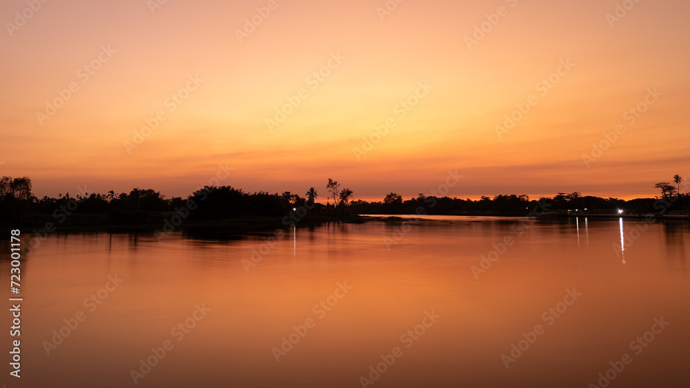 Beautiful view of the orange sunlight during sunset time in the golden hour with river on foreground.