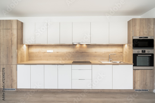 A Modern kitchen with white cabinets  wooden accents  a built-in oven  under-cabinet lighting  and a minimalist countertop.