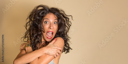 Mujer joven en actitud divertida saltando con cara de sorpresa sobre un fondo de color dorado