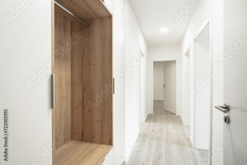 A Clean, modern hallway with wooden floors, white walls, an open wooden closet, and opened doors. It’s bright and inviting.