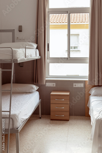 A clean and minimalistic hostel room with a bunk bed, white bedding, and a small wooden bedside table, ideal for budget travelers seeking affordable accommodation. Cheap hostels, save money.