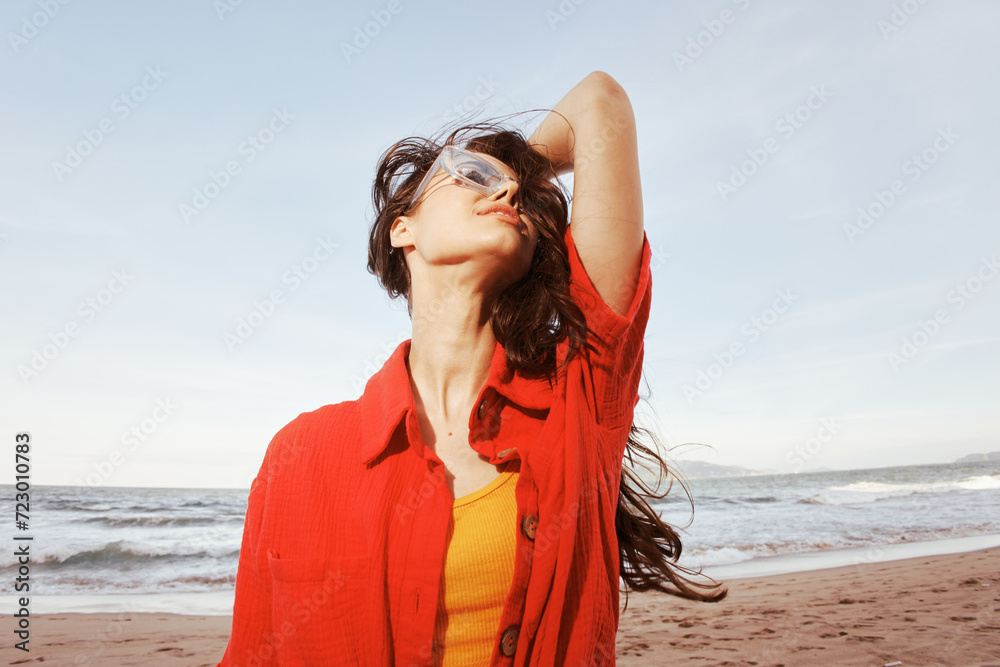 Cheerful woman with a big smile, wearing sunglasses and trendy red clothing, posing for a portrait on a sandy beach at sunset. Cheerful woman with a big smile, wearing sunglasses and trendy red clothing, posing for a portrait on a sandy beach at sunset.